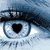 A blue eye with a black heart-shaped pupil, a book with green ribbon forming a heart, and a glass heart on a stand.