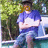 A person in a blue shirt and jeans sits on a boat with arms crossed, surrounded by green foliage.