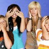 Four people pose against a solid blue background, with two individuals making hand gestures near their faces.