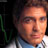 Pixelated static image of a person's face with light skin tone, dark hair, and neutral expression against dark background with green elements on left side.