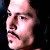 Pixelated close-up of a person's face with dark hair, mustache, and visible ear against a dark background.