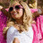 A pixelated image of a person with long blonde hair wearing sunglasses and a white top, set against a bright pink background with text elements.