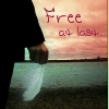 A person in dark clothing stands on a beach at sunset, holding a white object, with 'Free at last.' text overlaid on the sky.