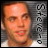 A pixelated portrait of a person with light skin and short brown hair, wearing a white shirt, against a gray striped background with vertical text.