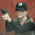 Pixelated figure in dark cap and shirt holds a black handgun, set against a reddish-brown background.