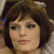 Pixelated close-up of a person with short dark hair and light skin, wearing a dark top with a light collar, against a blurred background.