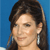 A static pixelated image of a person with dark brown hair styled in an updo, wearing a large silver earring against a solid blue background.