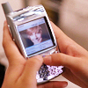 A person holds a silver flip phone with a small screen displaying a photo of a person with light brown hair and a dark shirt, while typing on the keypad.