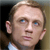Pixelated close-up of a person's face with light brown hair, blue eyes, and a neutral expression, wearing a white shirt against a dark background.
