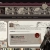 Static pixelated image showing a white rectangular interface with dark and red elements, set against a gray background with indistinct shapes.