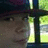 Pixelated static image showing a partial face with dark hair and a greenish background, likely a cropped section of a larger icon.