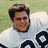 Pixelated image of a person with short brown hair wearing a white shirt featuring dark blue circular symbols on the chest.