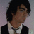 Static image of a person with dark hair wearing a black jacket over a white shirt and bow tie against a light purple background.