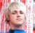 Pixelated static image of a person with light hair and closed eyes, wearing blue clothing against a pink-and-white background.