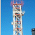 Tall vertical structure with layered sections against blue background, featuring red and brown accents and pixelated details.