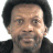 A pixelated image of a person with short dark hair and light skin, wearing a dark jacket over a gray shirt against a white background.