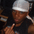 A person wearing a silver durag and black sleeveless shirt points with their right hand in three showing slight head movement