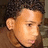 Pixelated close-up of a person's face with light skin tone, dark hair, and brown clothing against a blurred background.