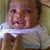 A child in a white shirt smiles with hands near the face, displayed in a four