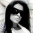 Pixelated static image of a figure with long black hair, white face, and dark clothing against a light background.