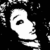 Pixelated black-and-white image of a stylized face with a single large eye, visible eyebrow, and partial hair, set against a dark background with scattered light pixels.