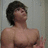 Pixelated static image of a shirtless person with dark hair, facing right against a light gray background.