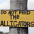 A static pixelated image shows a yellow sign with black text reading "DO NOT FEED THE ALLIGATORS" on a pole against a light sky background.