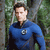 Pixelated image of a person in a blue long-sleeve shirt with a circular emblem on the chest, standing against a blurred green and brown background.