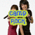 Two people stand on a beach holding signs reading 'camp rock' with waves and a starfish in the foreground.