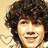 Pixelated portrait of a person with voluminous dark curly hair, light skin tone, and visible facial features against a pale background.