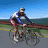 Animated sequence of two cyclists riding on a road with blue sky and green landscape background.