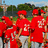 Group of people in red uniforms with white text on shirts, standing outdoors under a blue sky.