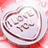 A heart-shaped candy with 'I LOVE YOU' embossed on it, displayed on a pink background with purple text reading 'Luv Yhoo Livah Your Ma Oldah'.
