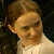 Pixelated close-up of a person's face with light brown hair and fair skin, wearing a white collared shirt against a dark background.