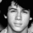 Static grayscale pixelated image of a person's face with closed eyes, neutral expression, and visible ear, set against a dark background.
