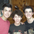 Three people pose together in a pixelated photo with pink text labels identifying them as 'Nick the shy cute one', 'Joe the funny cute one', and 'Kevin the romantic cute one' on a black background.