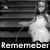 Black-and-white pixelated image of a figure in white attire holding an object, with the word 'Remember' at the bottom.