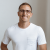 Pixelated image of a person wearing a white short-sleeve shirt against a light gray background.