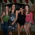 Four figures in casual clothing pose together against a dark background with indistinct shapes.