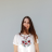 A pixelated figure with long brown hair wears a white shirt featuring a red and gray floral design against a light gray background.