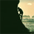 Pixelated static icon showing partial view of a light-colored figure with dark hair against a gradient background transitioning from dark green to beige, with visible pixelation and dithering effects.