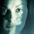 Pixelated close-up of a person's face with light blue and white tones, dark hair visible on the left side, and a blurred background.