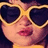 Pixelated close-up of a person wearing large dark sunglasses with gold frames, pink lips, and a yellow top against a dark background.