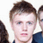 Pixelated static image of a person with short brown hair, light skin, and blue eyes wearing a dark blue shirt against a white background.