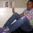 A pixelated image shows a person sitting with legs crossed, wearing blue jeans and a multicolored shirt, holding up an object against a light background.