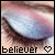 A 50x50 pixel animated buddy icon showing a close-up of an eye with pink and blue eyeshadow, displaying two frames where the left frame includes a heart symbol below "believer" text while the right frame omits it.