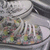 Pixelated static image with indistinct shapes and muted colors including gray, white, green, brown, pink, and black; no clear subjects or text visible.