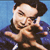 Pixelated image of a person with dark hair wearing a dark jacket, making a hand gesture near their face against a blue background.
