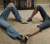 A pixelated image shows two figures in blue jeans and light skin tones forming a heart shape with their bodies on a beige floor, background includes dark furniture.