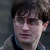 Pixelated close-up of a person with dark hair and glasses, wearing a light-colored jacket over a dark shirt against a muted background.